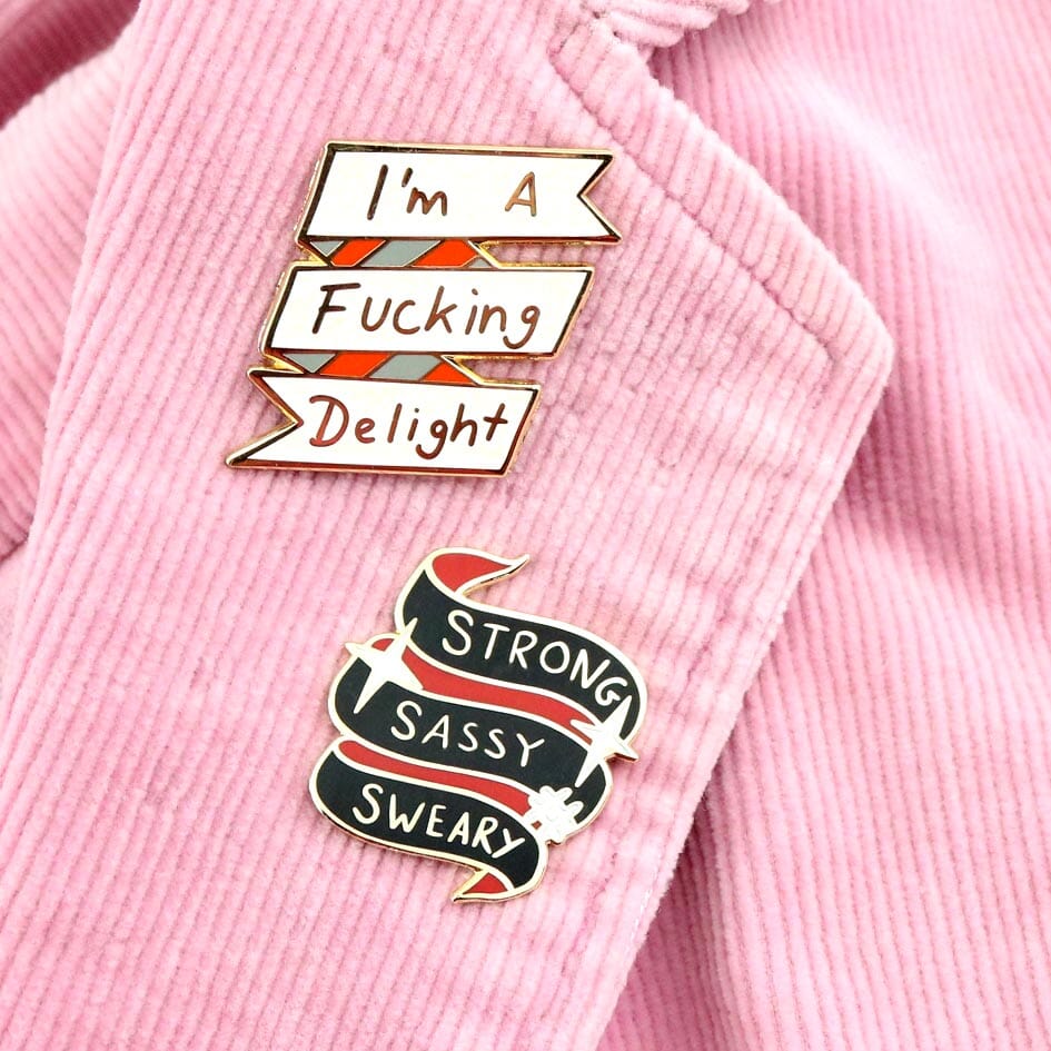 Hard enamel lapel pins on a pink jacket. The first lapel pin reads I'm A Fucking Delight. The second reads Strong Sassy Sweary.