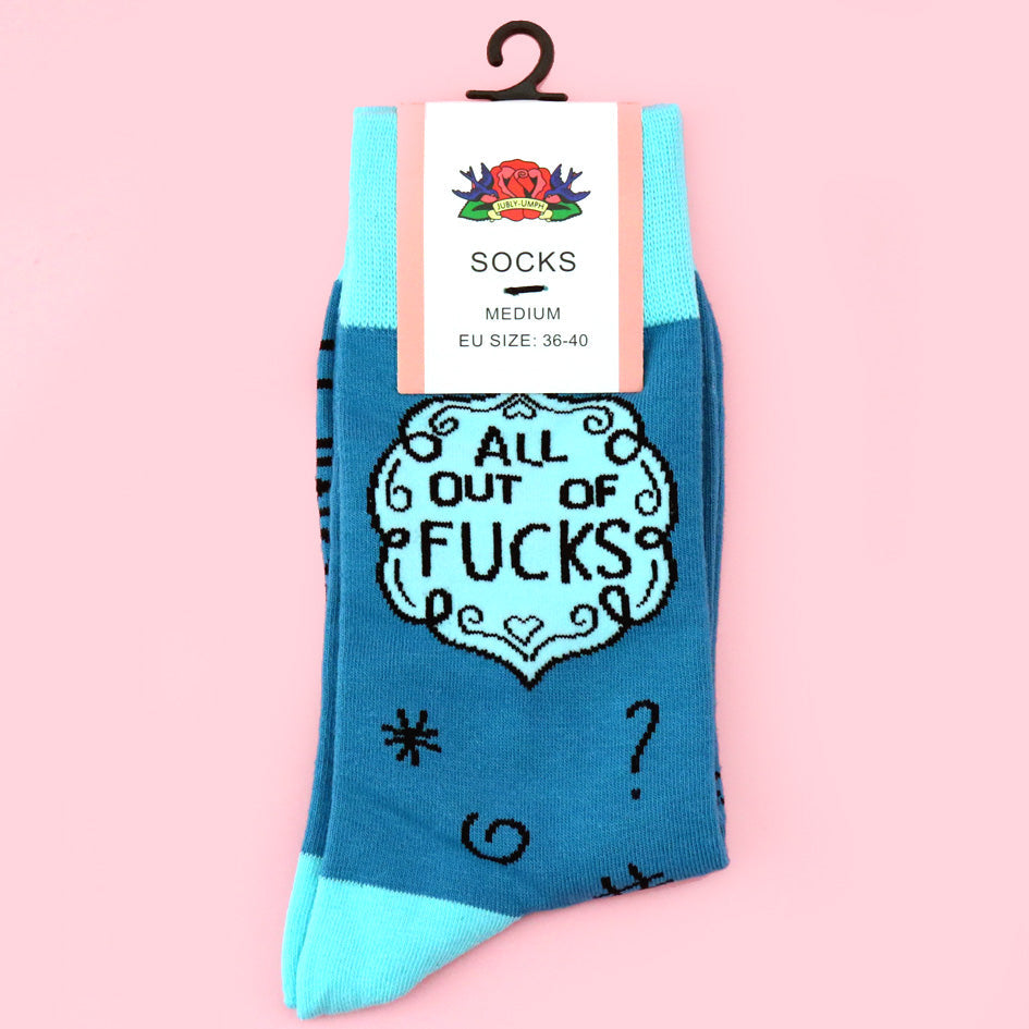 A pair of socks laying flat against a pink background in packaging displaying size medium. The socks are blue and light blue and read All Out Of Fucks.