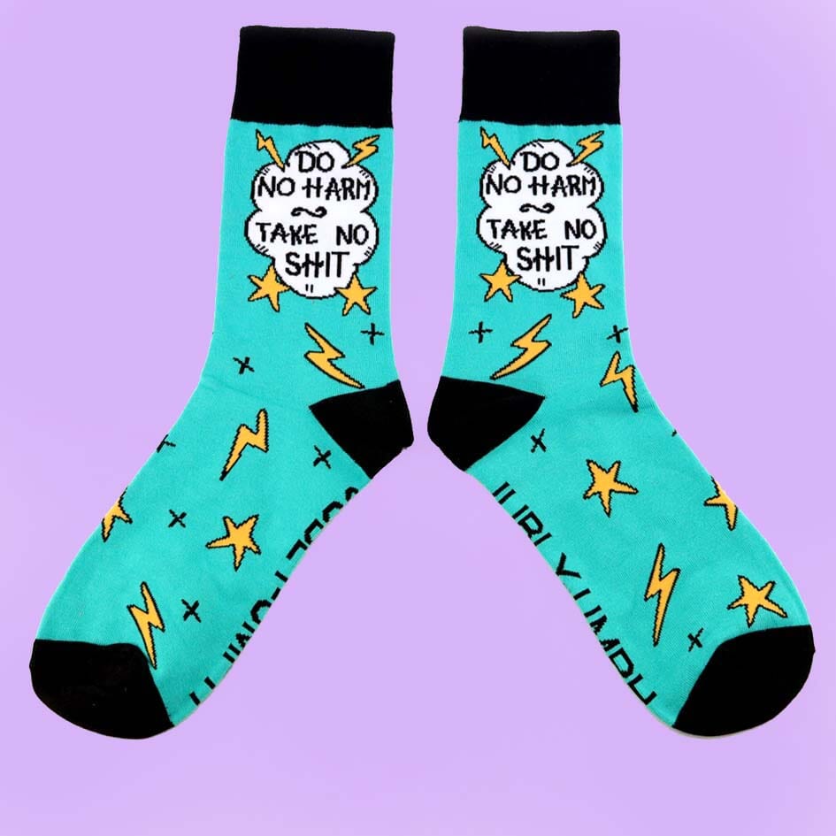 A pair of socks on a purple background. The socks are teal and black and read Do No Harm Take No Shit.
