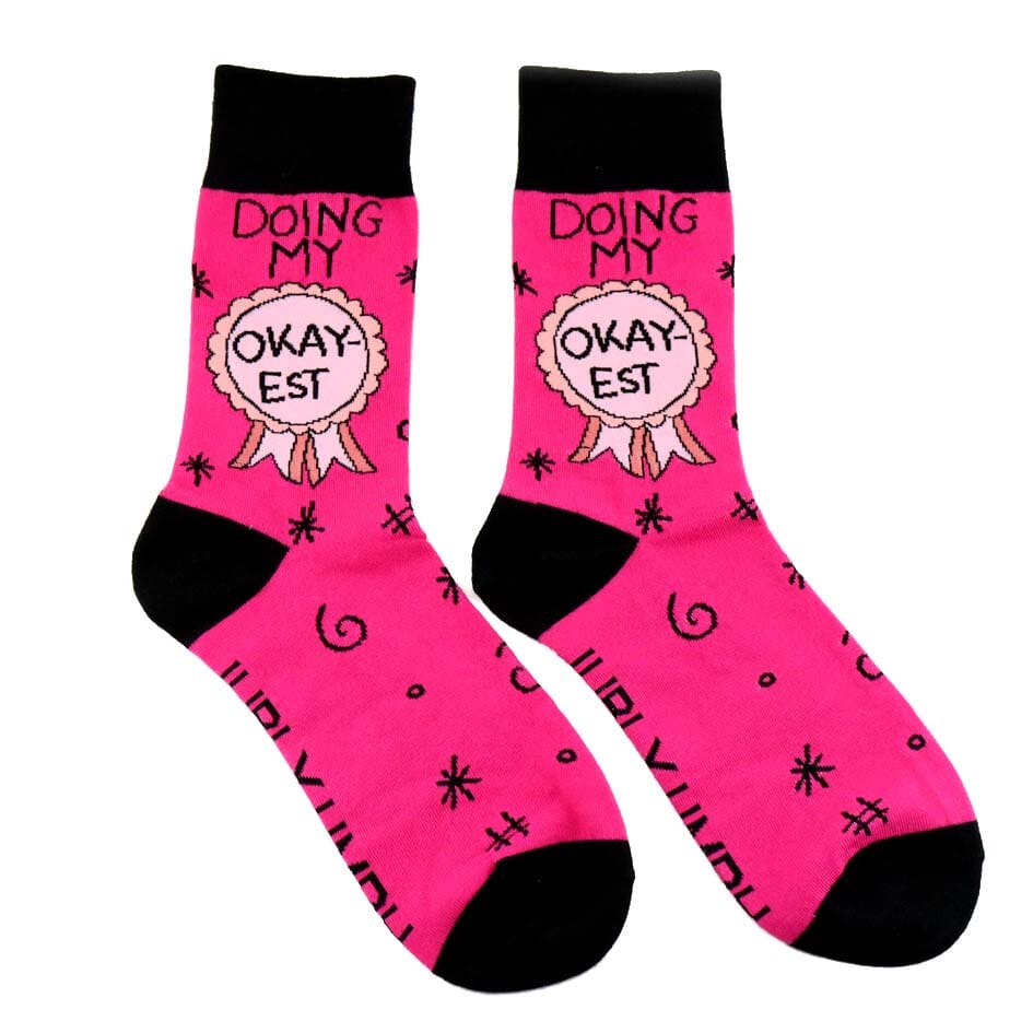 A pair of socks on a white background. The socks are pink and black and read Doing My Okay-est.