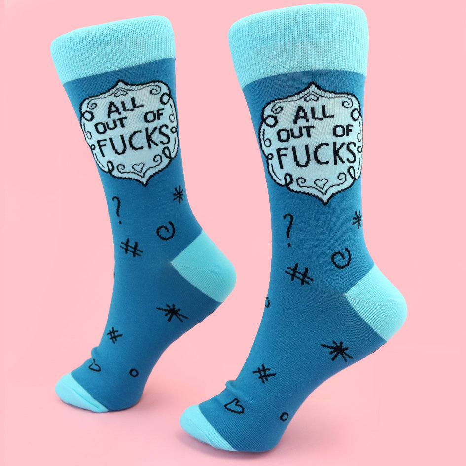 A pair of socks standing against a pink background. The socks are blue and light blue and read All Out Of Fucks.