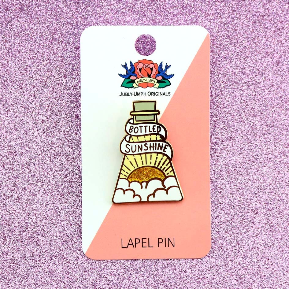 A hard enamel lapel pin on Jubly-Umph cardstock. The pin is in the profile of a beaker with a yellow glitter sun. The pin says Bottled Sunshine.