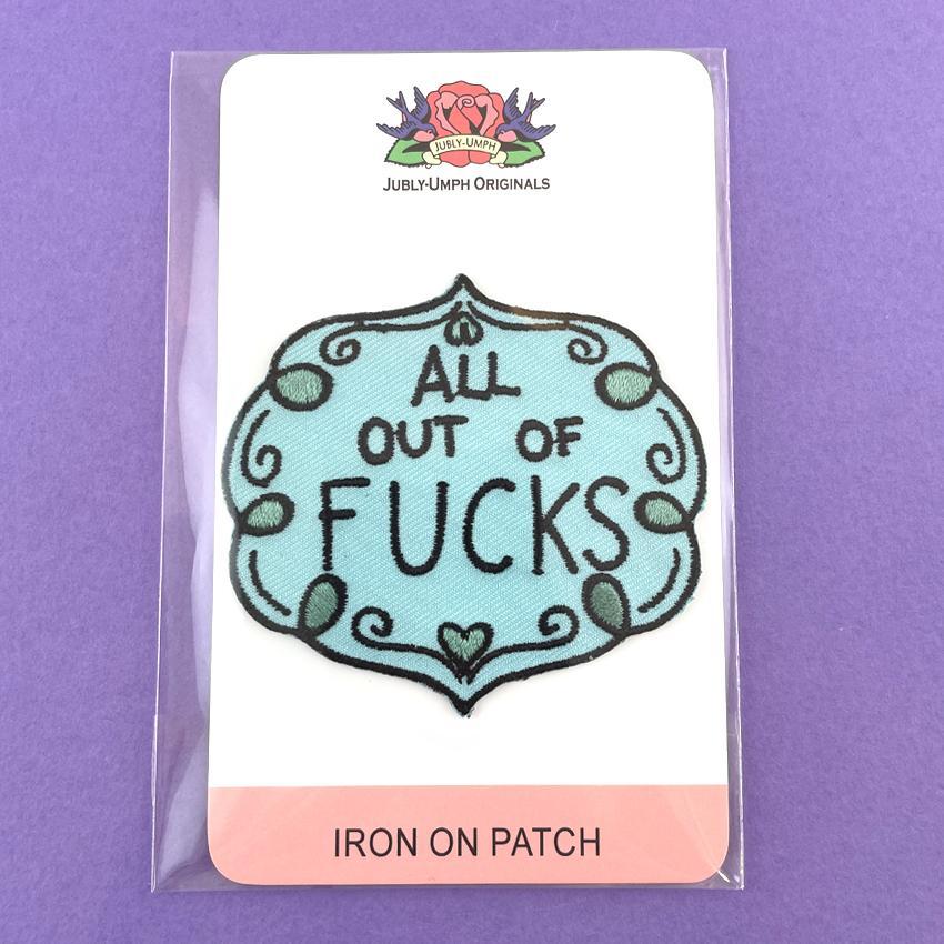An iron on embroidered patch  on Jubly-Umph cardstock against a purple background. The patch is blue and green and reads All Out Of Fucks.