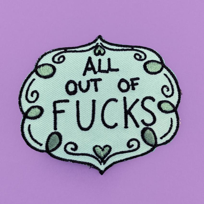 An iron on embroidered patch  against a purple background. The patch is blue and green and reads All Out Of Fucks.