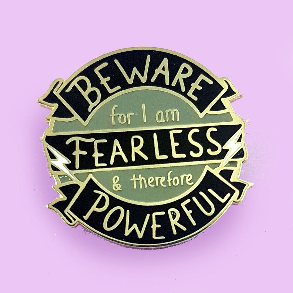round black and grey enamel lapel pin with the words beware for I am fearless and powerful on it, with two small lightning bolts.