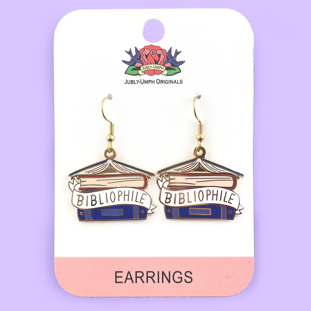 A pair of dangle earrings displayed on Jubly-Umph cardstock. The earrings say Bibliophile in the middle of a stack of blue books.
