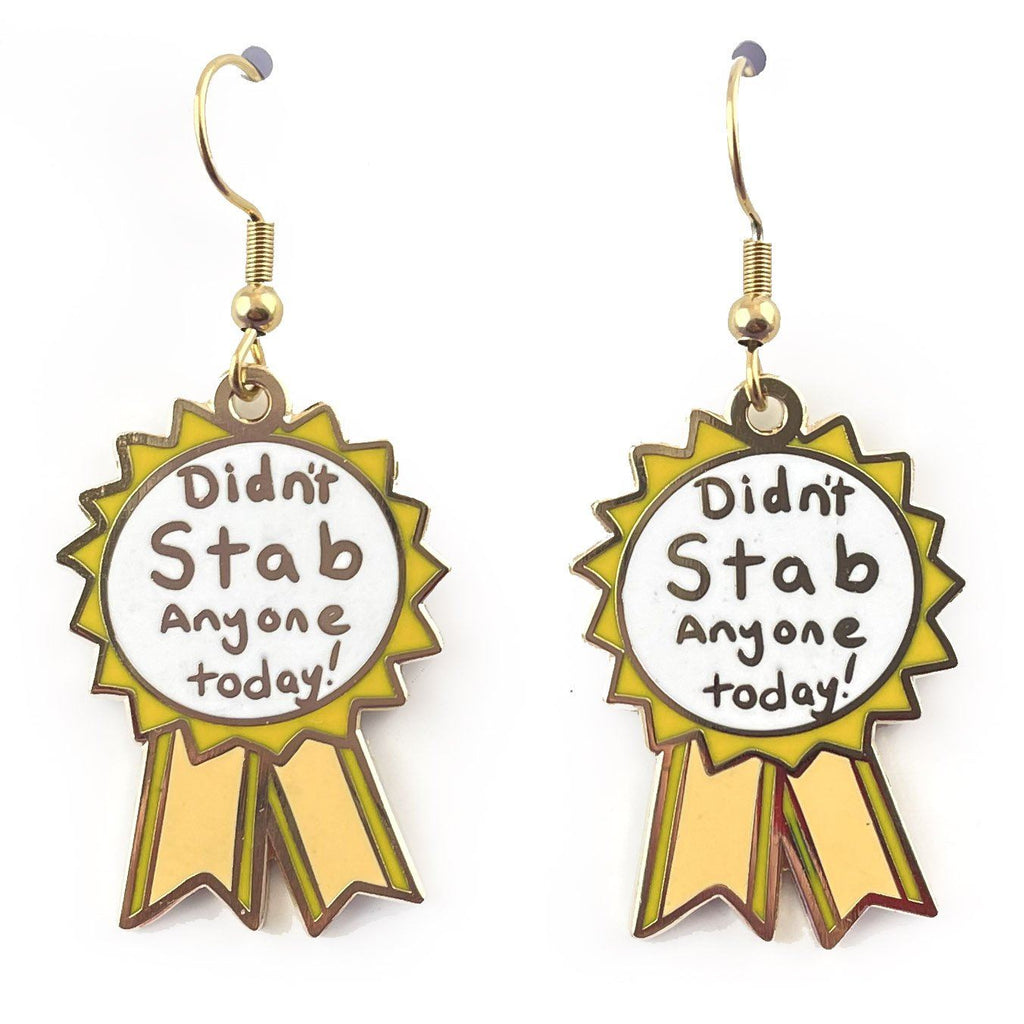 A pair of dangle earrings in the shape of an award ribbon. They are on a white background. The ribbon is yellow and white, and reads Didn’t Stab Anyone Today!