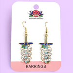 A pair of earrings displayed on Jubly-Umph card stock. The earrings are in the shape of dagger and read Fighting Invisible Battles.