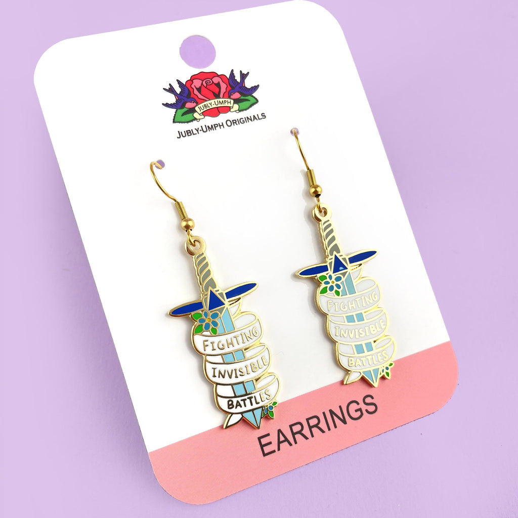 A pair of earrings displayed on Jubly-Umph card stock. The earrings are in the shape of dagger and read Fighting Invisible Battles.