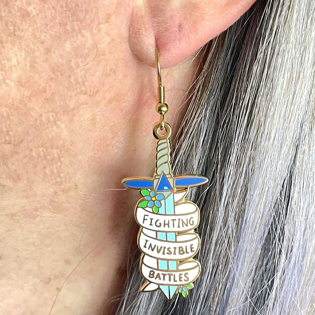 The earrings are in the shape of dagger and read Fighting Invisible Battles.