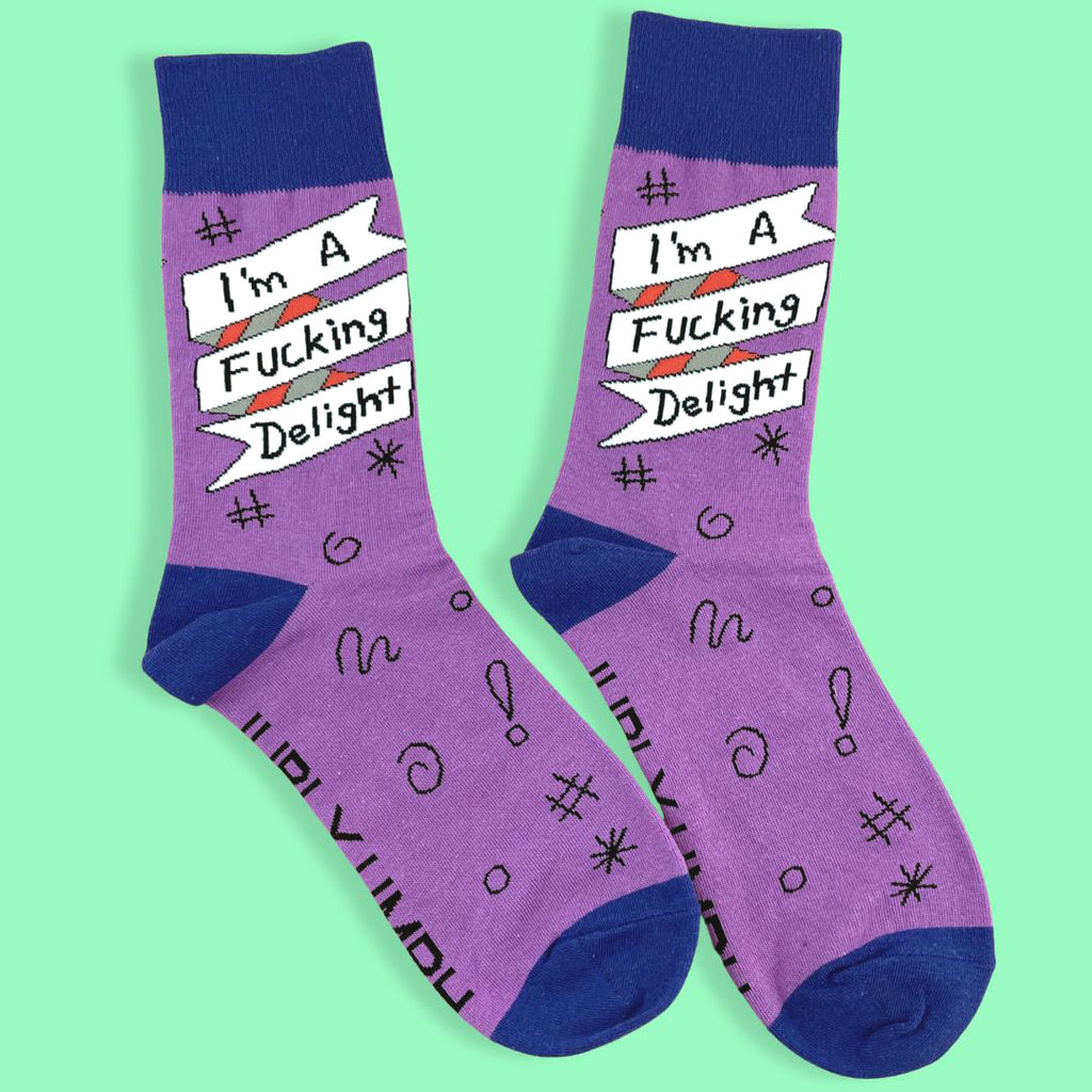 A pair of socks standing against a green background. The socks are purple and blue and read I'm A Fucking Delight.