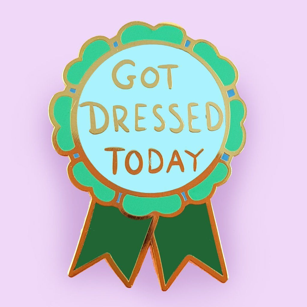 A hard enamel lapel pin on a purple background. The pin is in the shape of a green award ribbon. The pin reads Got Dressed Today.