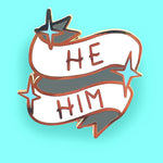 A hard enamel lapel pin on a blue background. The pin reads He Him.