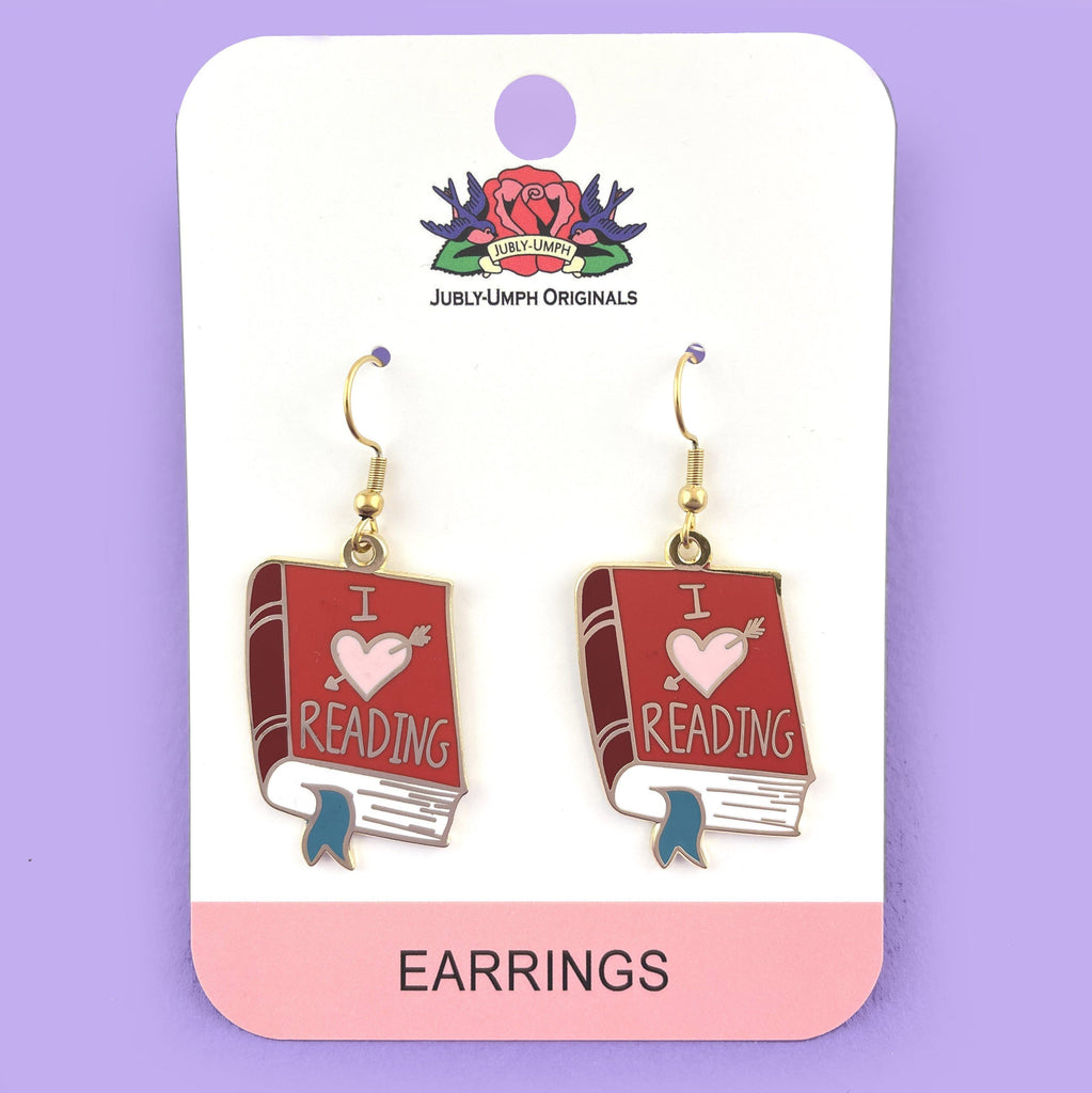 A pair of earrings displayed on Jubly-Umph card stock. The earrings are in the shape of a red book. The earrings read I (heart image) reading.
