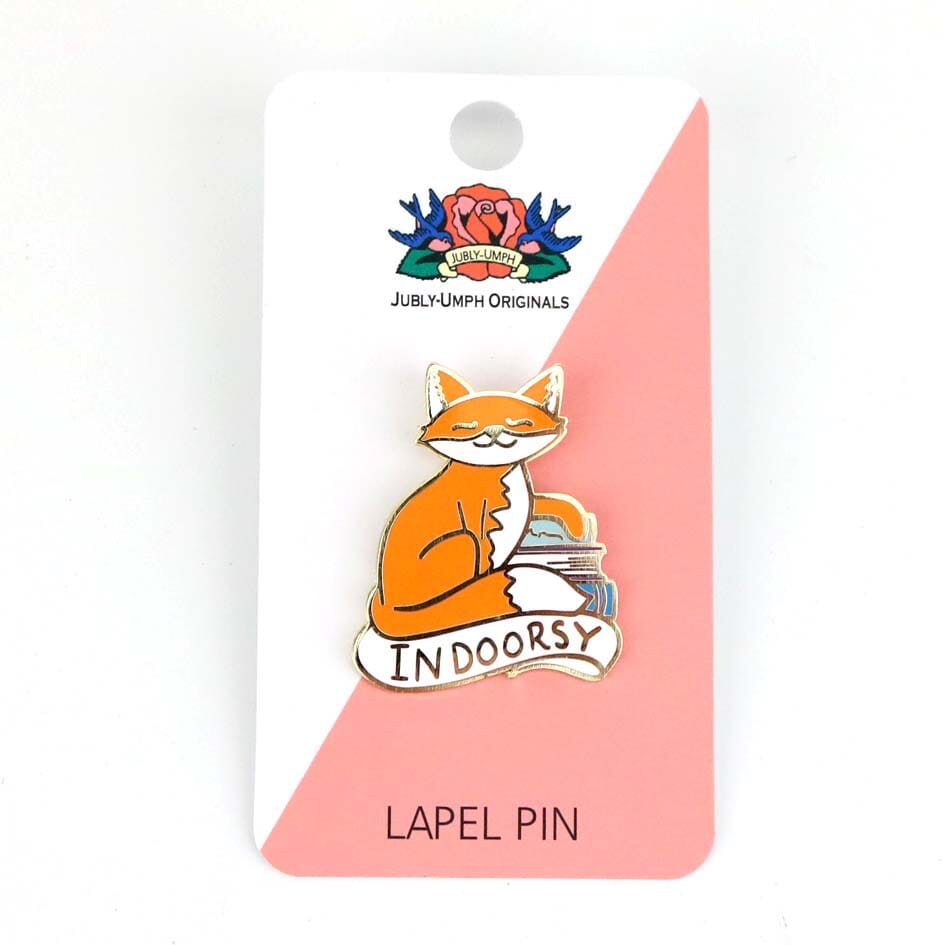 A hard enamel lapel pin being displayed on a Jubly-Umph backing card. The lapel pin is in the shape of an orange cat and reads Indoorsy.