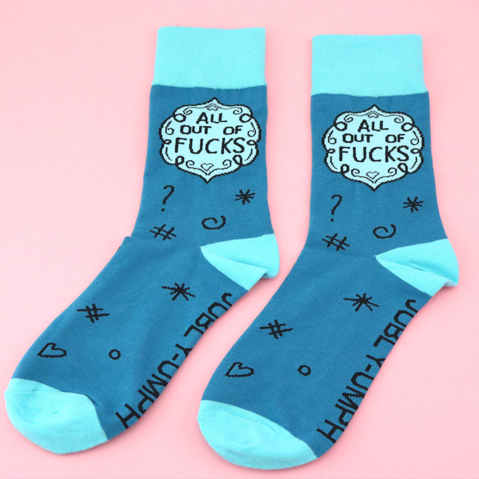 A pair of socks laying flat against a pink background. The socks are blue and light blue and read All Out Of Fucks.