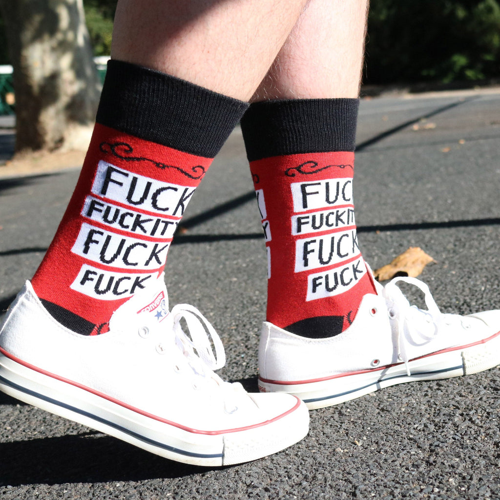 A pair of socks being worn with white shoes. The socks are red and black and read Fuck Fuckity Fuck Fuck.